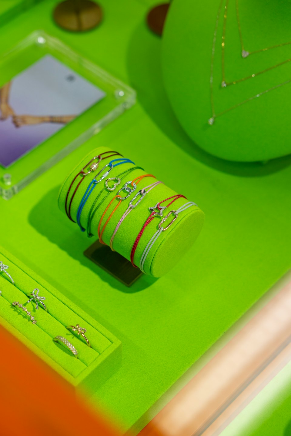 Colorful string bracelets and gold jewelry displayed on green stands.
